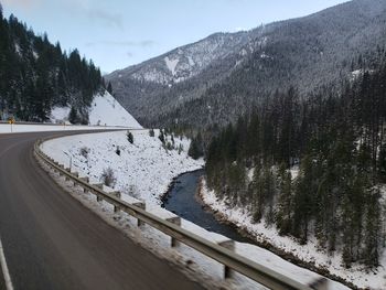 Snow covered road by trees against sky