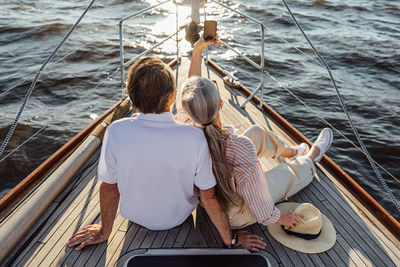 Rear view of friends sitting on boat sailing in sea