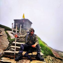 Man sitting on rock against sky