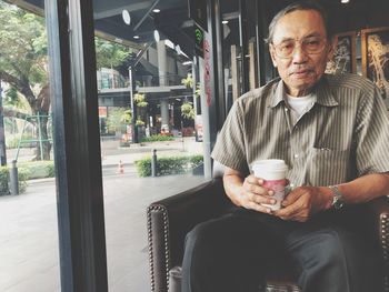 Portrait of senior man holding disposable cup at home