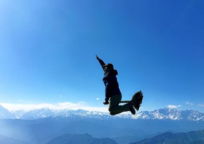 Man with arm raised sitting on broom against sky