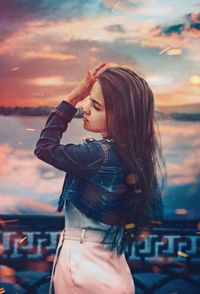 Side view of young woman standing against sky at sunset