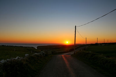 Road by sea against clear sky during sunset