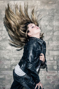 Portrait of girl tossing hair standing against wall