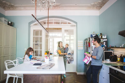 Smiling woman carrying son while talking to man standing in kitchen at home