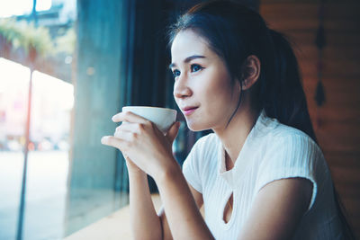 Close-up of young woman looking away while having coffee at cafe