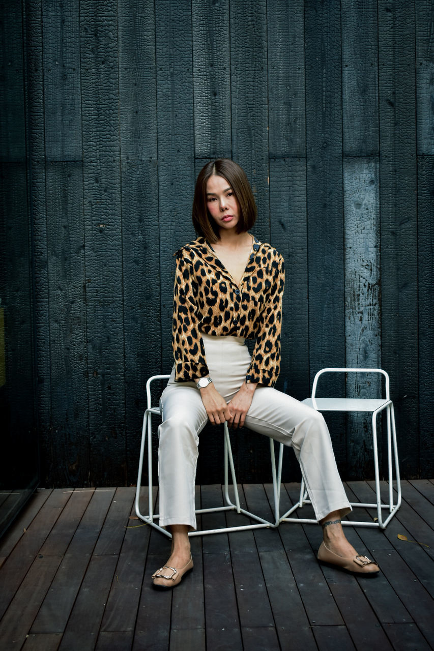 sitting, one person, adult, seat, women, chair, portrait, full length, fashion, young adult, person, clothing, front view, looking at camera, photo shoot, hairstyle, spring, furniture, female, wood, emotion, relaxation, footwear, long hair, brown hair, dress, indoors, casual clothing, lifestyles, copy space, smiling, portrait photography, white, contemplation, black, pattern