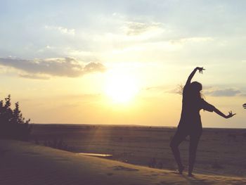 Silhouette woman dancing on field against sky during sunset