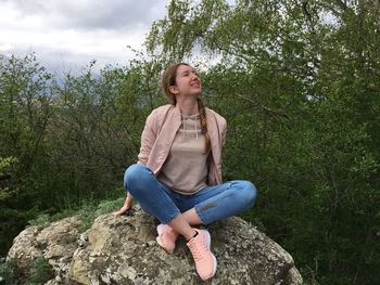 Young woman sitting on rock against trees