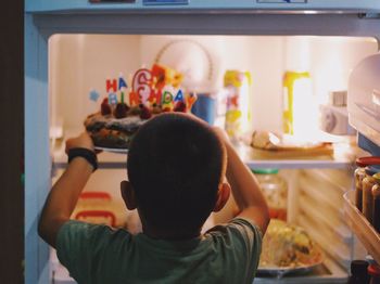 Rear view of boy putting cake in refrigerator