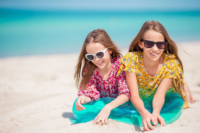 Portrait of smiling sisters wearing sunglasses with inflatable ring lying at beach