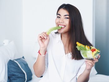 Cheerful young woman holding salad bowl against wall at home