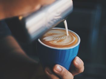 Close-up of hands pouring milk in coffee