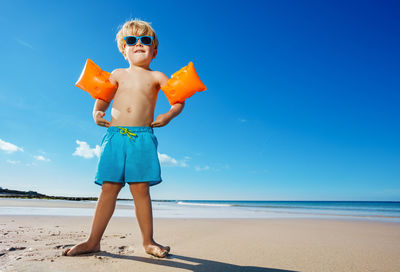 Rear view of woman with arms outstretched standing at beach against blue sky