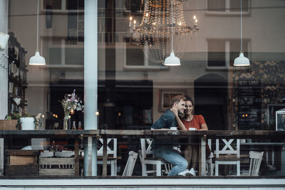 Young woman with arm around on man sitting by cafe window