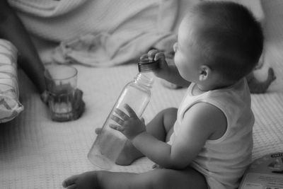 Cute baby boy sitting on bed and playing with a water bottle