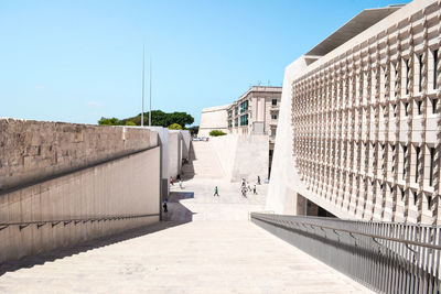 Footpath amidst buildings against clear blue sky