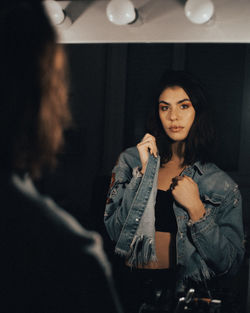 Woman wearing denim jacket while standing in front of mirror