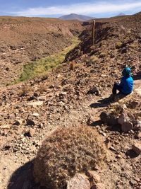 Rear view of man sitting on rock against sky