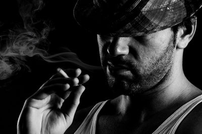 Close-up of man smoking cigarette against black background