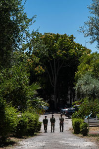 People walking on road amidst trees in city against sky