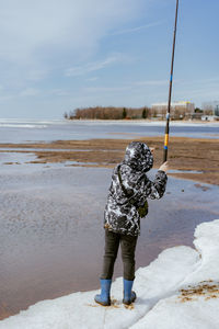 Cute little caucasian boy holding a fishing rod looking into distance on sea side on spring day