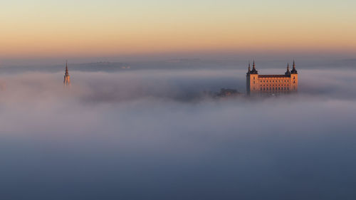 Buildings amidst fogs against sky during sunset