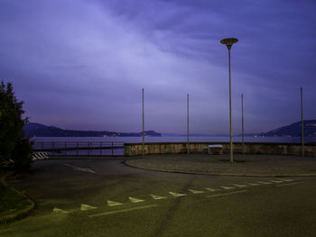 Street lights by bridge against sky at dusk