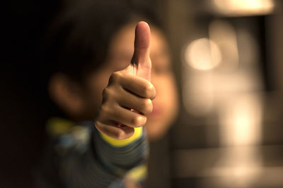 Close-up of child gesturing thumbs up sign in darkroom