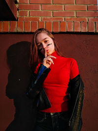 Portrait of beautiful young woman standing against brick wall