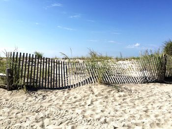 Broken fence on sand at beach against sky