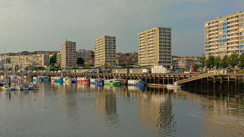 Boats moored in river by buildings against sky in city