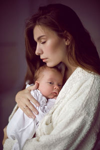 Mother in a white robe holds a small newborn daughter against the wall in the bedroom