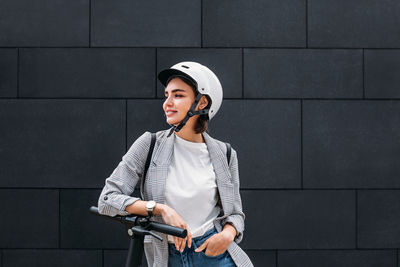 Young woman looking away while standing against wall