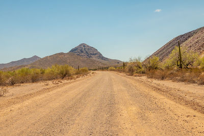 Dirt road leading towards mountains against clear sky