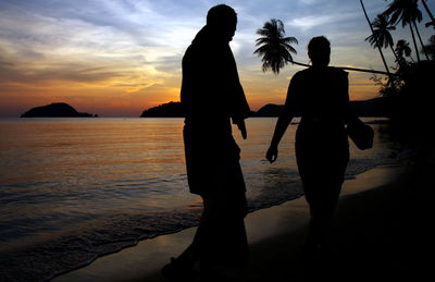 Silhouette people walking at beach against sky during sunset