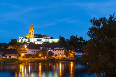 Illuminated buildings by river against sky at dusk