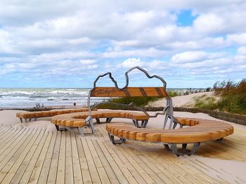 Lounge chairs by swimming pool at beach against sky