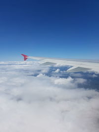 Cropped image of aircraft wing over clouds against blue sky