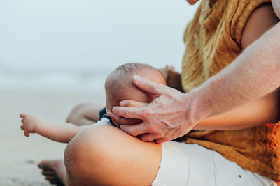 Cropped image of father touching hand of mother while holding baby outdoors