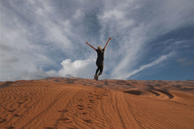 Rear view of person jumping on sand at desert