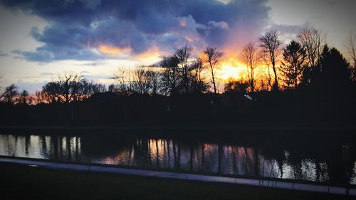 Silhouette trees by lake against sky during sunset