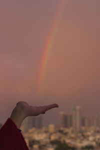 Close-up of hand against rainbow in sky