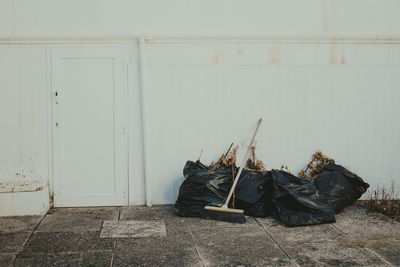 Broom and black garbage bags by white wall