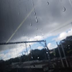 Close-up of wet window against sky