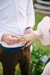 Midsection of groom putting ring in brides finger