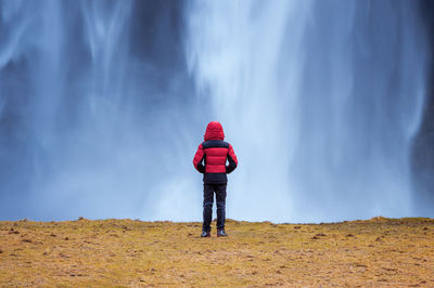 Rear view of man looking at waterfall falling from mountain