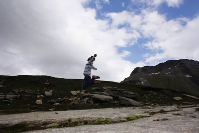 Side view of man standing on rock against sky