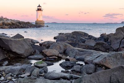 Lighthouse by sea against sky during sunset