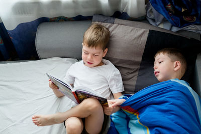Little brother reads a book on the bed for an elder. friendship between brothers. love for reading